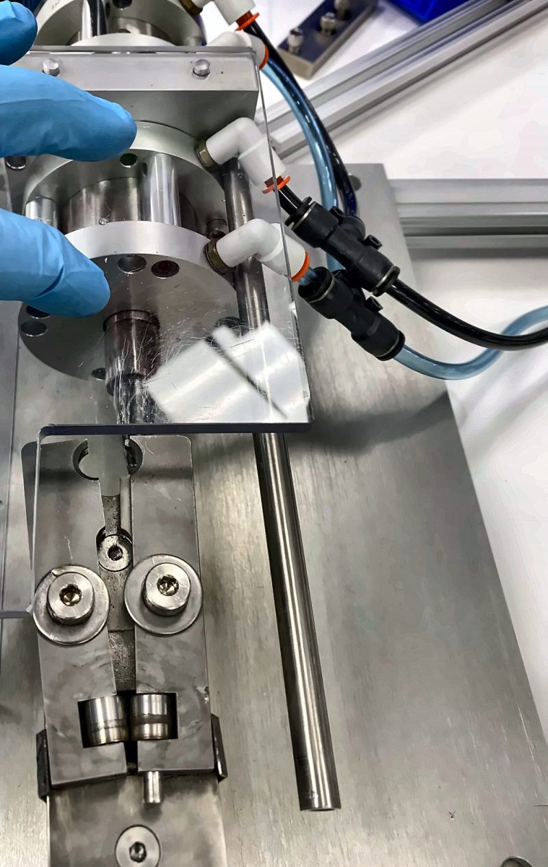 Gloved hand at a die station with rollers behind a clear guard